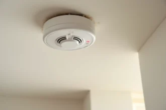 Détecteur de fumée blanc fixé au plafond avec voyant LED rouge clignotant dans un couloir de maison