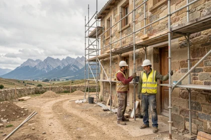 Chantier de rénovation d'un bâtiment en pierre dans les Pyrénées-Atlantiques avec des ouvriers sur échafaudage et les montagnes en arrière-plan